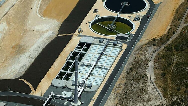 Aerial view of the Alkimos Wastewater Treatment Plant showing circular treatment tanks, process basins, pipelines, and operational infrastructure. The facility is situated within a landscaped industrial site, illustrating key components of modern wastewater treatment and water recycling operations.